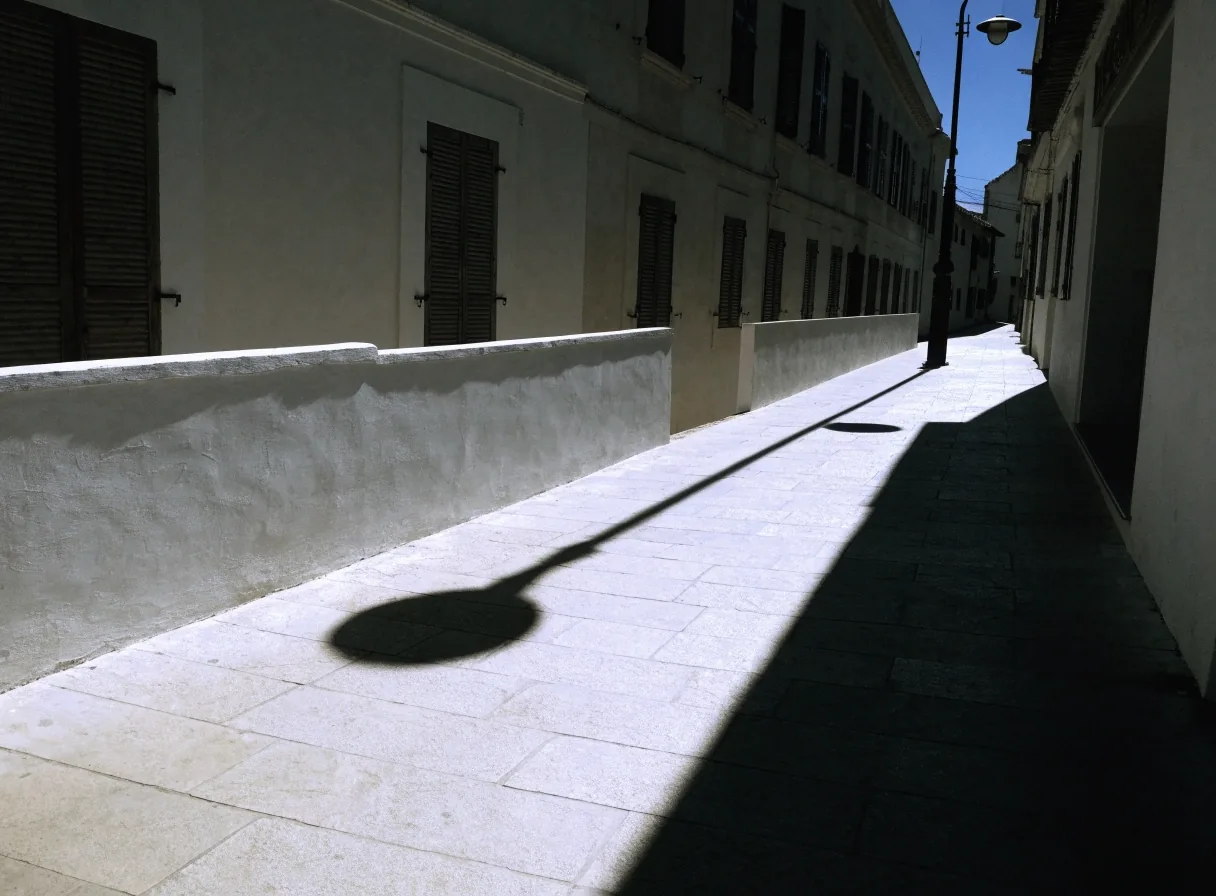 Acera vacía y muro encalado con una sombra dura al mediodía en una localidad española